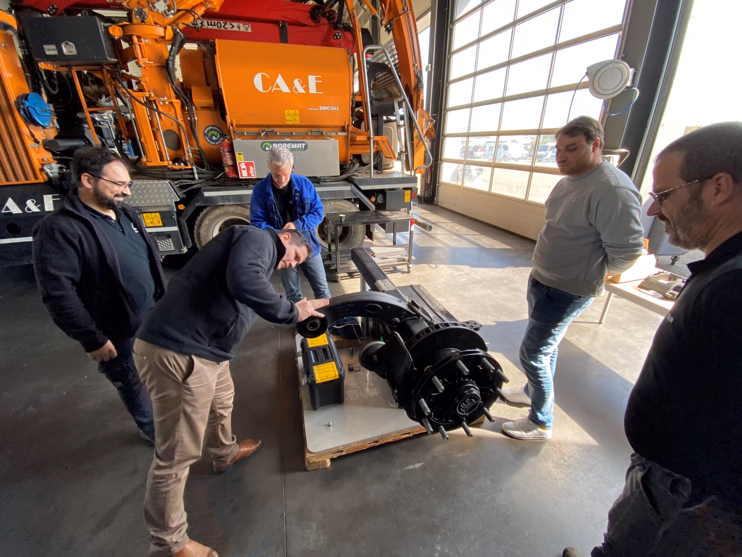 BPW-Formation in Carcassonne: Trainer und Techniker an einem zerlegten Lkw-Achskörper, Werkzeug und Bremsteile auf der Werkbank — Praxis-Tag in der Partnerwerkstatt Techno Poids Lourds.