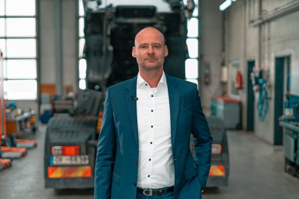 Norman Binde, Managing Director Sales bei Alltrucks, in einer Werkstatthalle vor einem aufgebockten Nutzfahrzeug