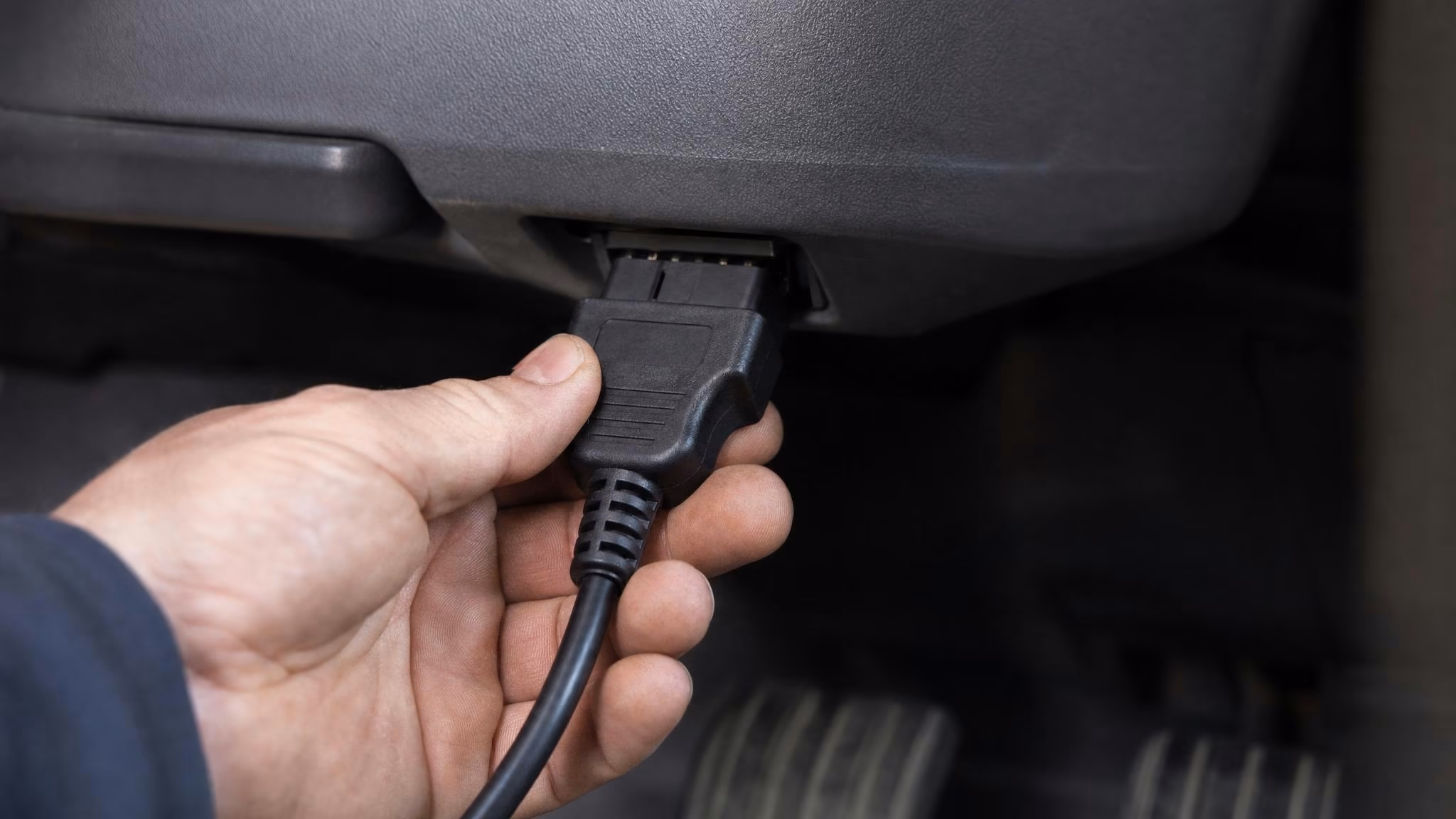 Hand steckt OBD-Adapter in den Diagnoseport unter dem Lenkrad — Einstieg in die Mehrmarkendiagnose.