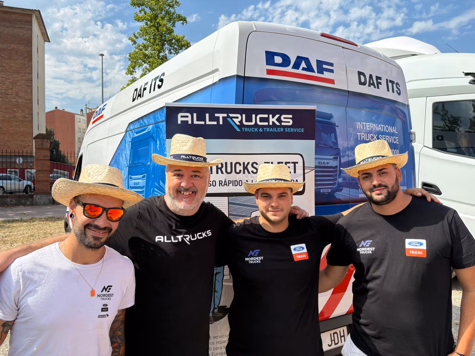 Keturi „Nordest Trucks“ ir „Alltrucks“ komandos nariai su šiaudinėmis skrybėlėmis priešais „DAF-ITS“ aptarnavimo automobilį ir „Alltrucks“ stendą Olote