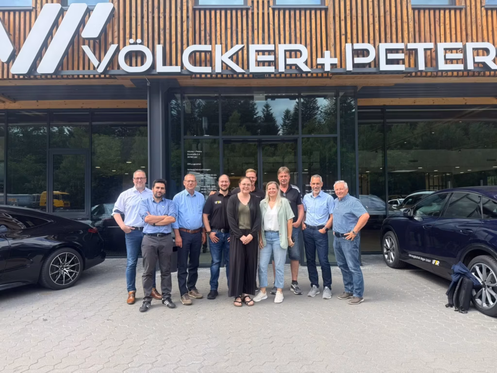 Członkowie rady partnerskiej Alltrucks wraz z Peterem Ortmannem, dyrektorem ds. sprzedaży Alltrucks na region DACH-NL, przed budynkiem firmy Völcker + Peters z drewnianą fasadą i napisem firmowym