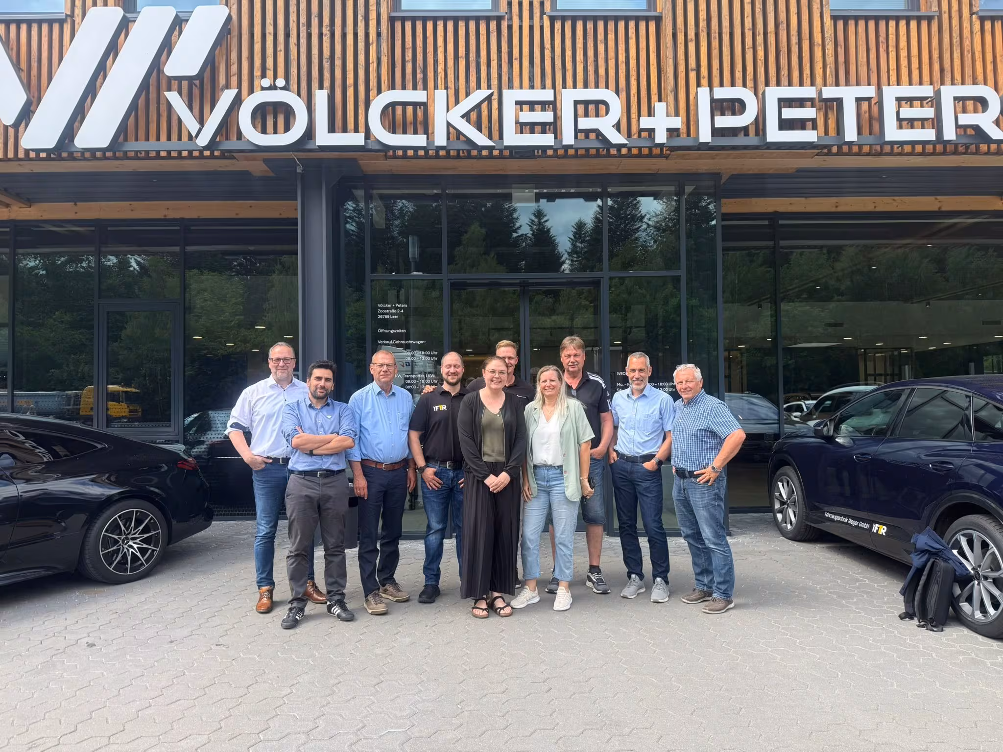 „Alltrucks“ partnerių patariamojo komiteto nariai su Peteriu Ortmannu, „Alltrucks“ pardavimų vadovu DACH-NL regione, priešais „Völcker + Peters“ pastatą su medine fasadu ir įmonės logotipu