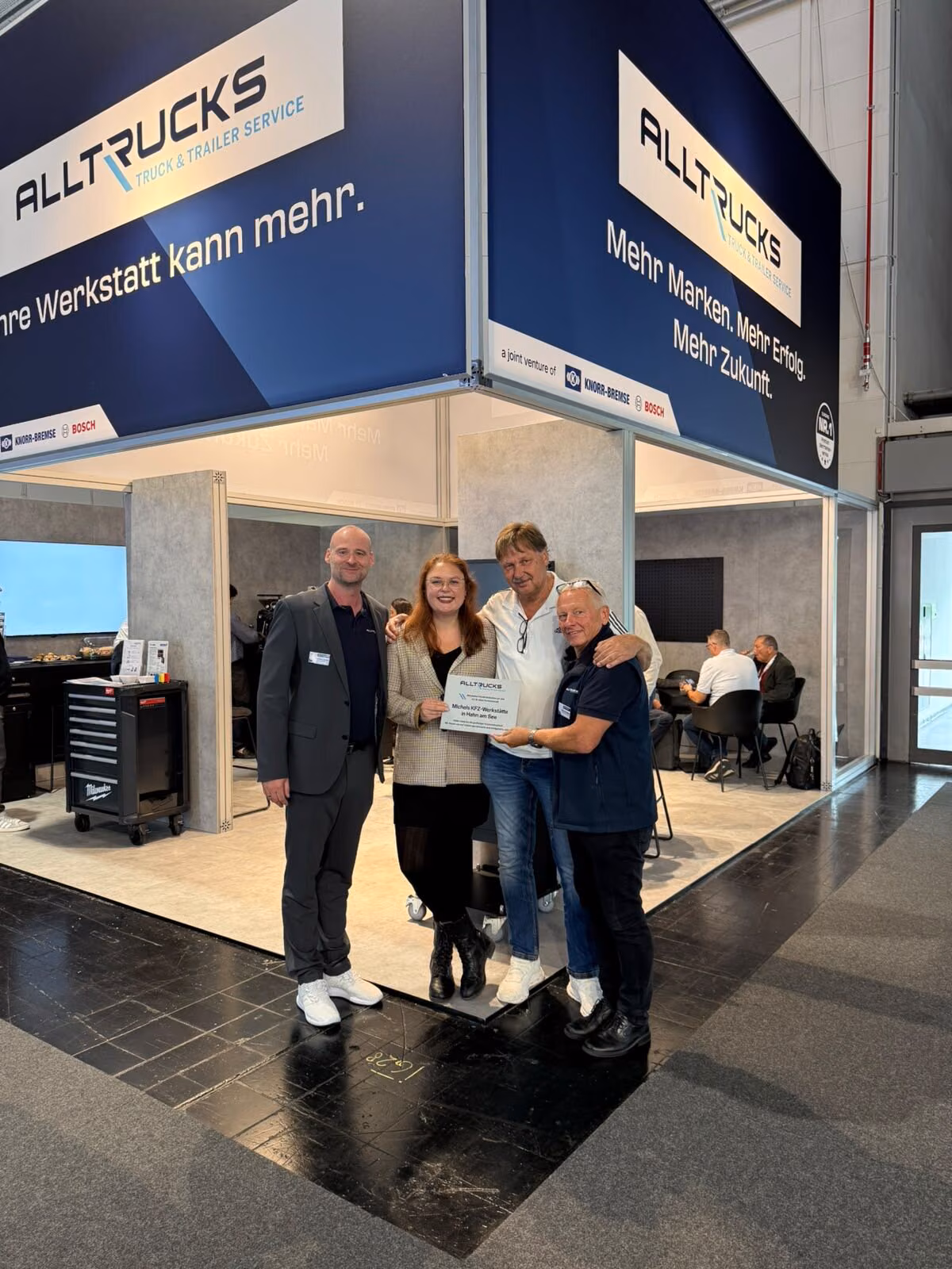 Cuatro personas con un certificado por sus diez años de relación, delante del stand de Alltrucks en la IAA Transportation 2026