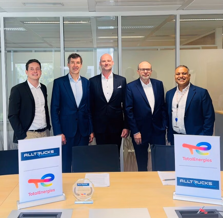 Cinco representantes de TotalEnergies Lubricants y Alltrucks posan detrás de una mesa con los logotipos de ambas empresas tras la firma del contrato